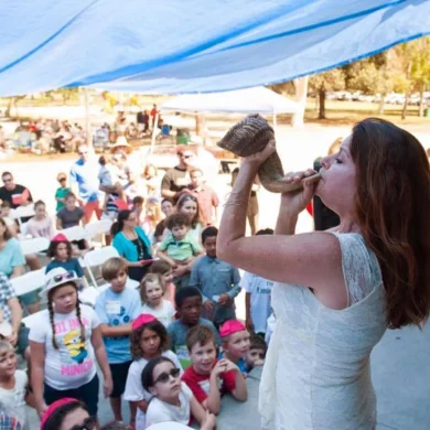 HaMo'Robyn Solovei blowing a shofar at an outdoor community gathering
