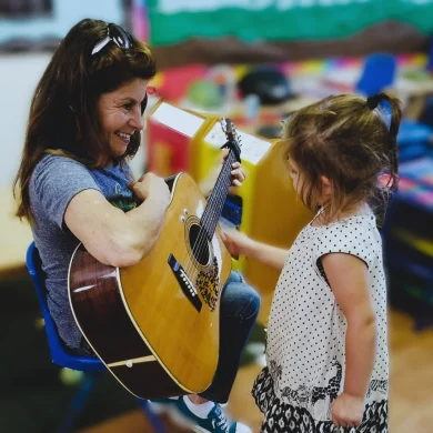 HaMo Robyn Solovei playing acoustic guitar with a young girl in preschool