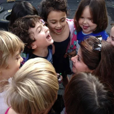 HaMo Robyn Solovei in a circle of children laughing and singing together