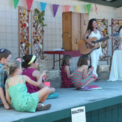 HaMo Robyn Solovei performing with guitar on an outdoor stage for children